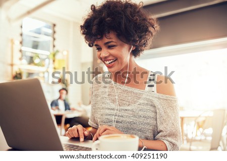 Image of happy woman using laptop while sitting at cafe. Young african american woman sitting in a coffee shop and working on laptop.
