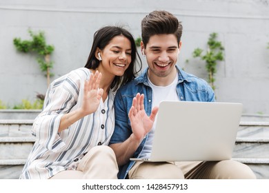 Image Of Happy Young Amazing Loving Couple Business People Colleagues Outdoors Outside On Steps Using Laptop Computer Waving Talking With Family Or Friends.