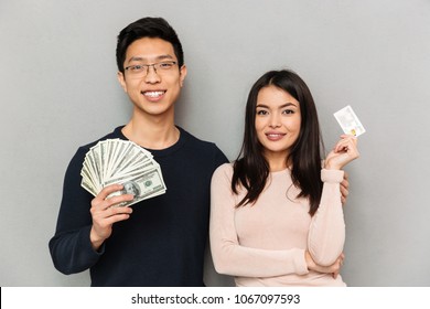 Image of happy young asian loving couple standing isolated over grey wall background holding money and credit card. - Shutterstock ID 1067097593