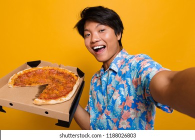 Image Of Happy Young Asian Man Standing Isolated Over Yellow Background Eat Pizza Take A Selfie By Camera.