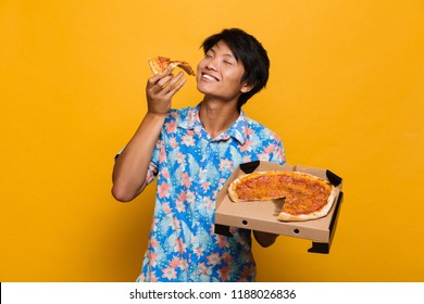 Image Of Happy Young Asian Man Standing Isolated Over Yellow Background Eat Pizza.