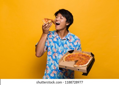 Image Of Happy Young Asian Man Standing Isolated Over Yellow Background Eat Pizza.