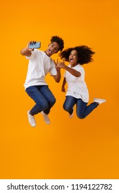 Image Of Happy Young Cute African Couple Jumping Isolated Over Yellow Background Make Selfie By Phone.