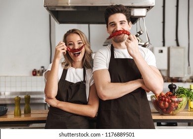 Image of happy young friends loving couple chefs on the kitchen having fun with pepper as a moustache. - Powered by Shutterstock