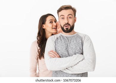 Image of happy young loving couple isolated over white wall background looking camera tell a secrets to each other.