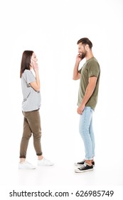 Image Of Happy Young Loving Couple Standing Isolated Over White Background. Looking Aside And Talking By Phones.