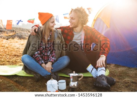 Image of happy young loving couple outside with tent in free alternative vacation camping over mountains drinking hot tea.