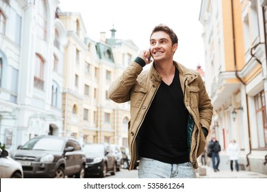 Image of happy young man walking on the street and looking aside while talking by his phone. - Powered by Shutterstock