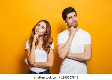 Изображение счастливых молодых людей мужчины и женщины в основной одежде мышления и трогательного подбородка, глядя в сторону изолированных на желтом фоне