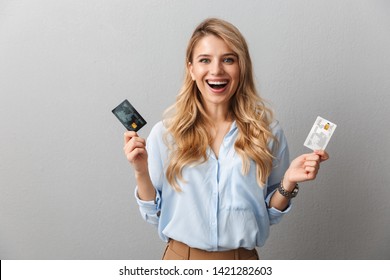 Image Of A Happy Young Pretty Blonde Business Woman Posing Isolated Grey Wall Background Holding Two Credit Cards.