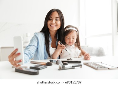 Image of happy young woman with little daughter at home indoors make selfie near table with cosmetics. స్టాక్ ఫోటో