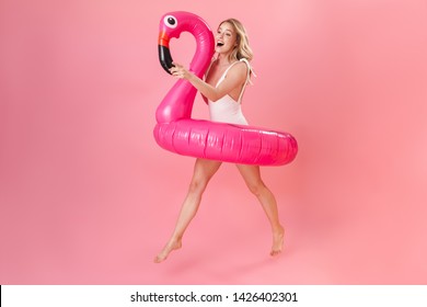 Image of happy young woman posing isolated over pink wall background dressed in swimwear holding flamingo rubber ring beach concept.