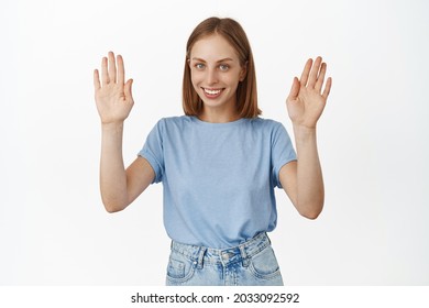 Image Of Happy Young Woman Smiling, Raising Hands Up In Surrender, Has Nothing, Showing Empty Palms, Standing In T-shirt Against White Background