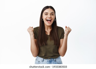 Image of happy young woman winning prize, making fist pump and smiling excited, triumphing as achieve goal, celebrating victory, shouting amazed, white background