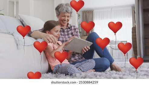 Image of heart balloons over happy caucasian grandmother and granddaughter using tablet at home. family, domestic life, love and care concept digitally generated image. - Powered by Shutterstock