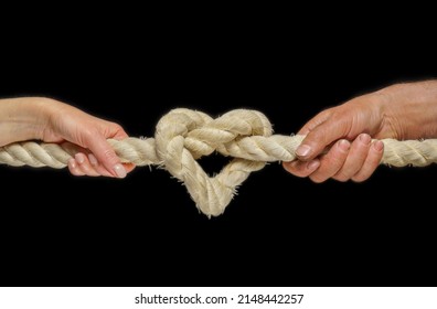  Image of a heart in the form of a rope knot. Male and female hands hold on to a thick rope. Knot tightening. The concept of strong love and inextricable relationship.                              