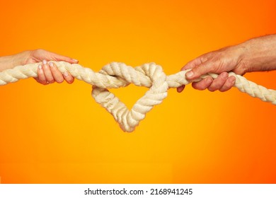 Image of a heart in the form of a rope knot. Male and female hands hold on to a thick rope. Knot tightening. The concept of strong love and inextricable relationship.                                