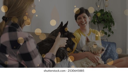 Image of hearts over caucasian female couple sitting on sofa with their pet dogs. Valentines, love and celebration concept digitally generated image. - Powered by Shutterstock