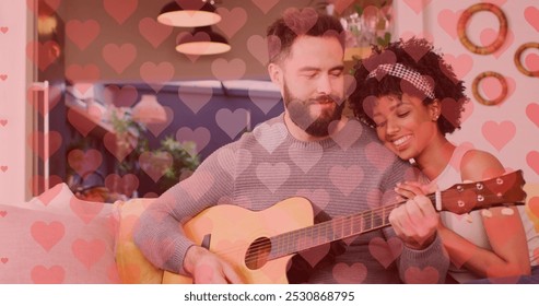 Image of hearts over happy diverse couple playing guitar. Love, romance, lifestyle and family time concept digitally generated image. - Powered by Shutterstock