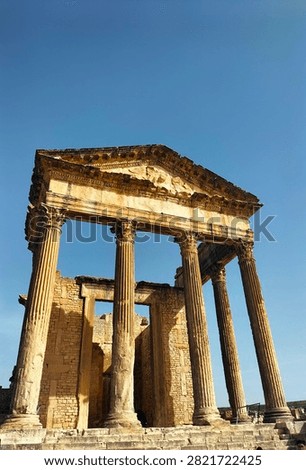 The image highlights the towering front portico of the magnificent Capitoline Temple (The Capitol) located at the archaeological.  four tall, monolithic Corinthian columns standing prominently in the foreground, supporting a beautifully preserved stone architrave, frieze, and a triangular pediment.
