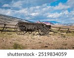 Image of a historic frontier wagon with wooden slat sides and wheels sits on the scenic landscape in Wyoming, USA.