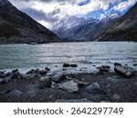 An image of a Hooker Lake from the rocky coast in the mountains under the cloudy sky