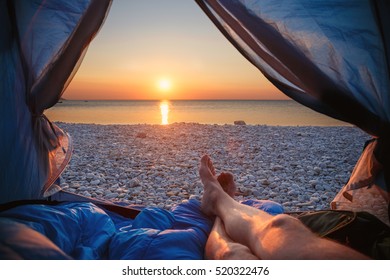 Image human legs lying in tourist tent with view of the sunset sea. Shallow DOF. Focus on pebble.