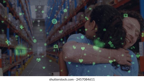 Image of icons floating over happy diverse female and male warehouse workers hugging. business, finance and delivery services concept digitally generated image. - Powered by Shutterstock