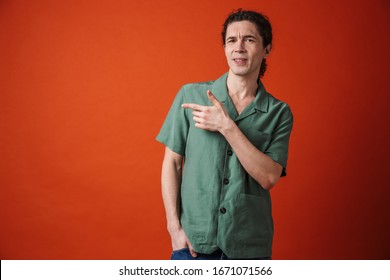 Image of irritated handsome man looking at camera and pointing finger aside isolated over orange background - Shutterstock ID 1671071566