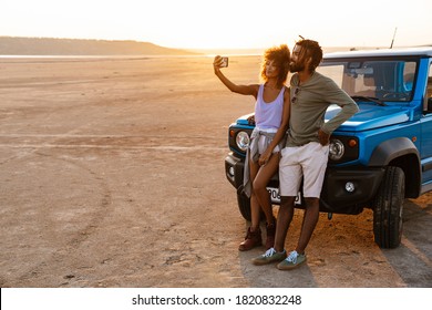 Image of joyful african american couple taking selfie on cellphone while travelling with car in desert