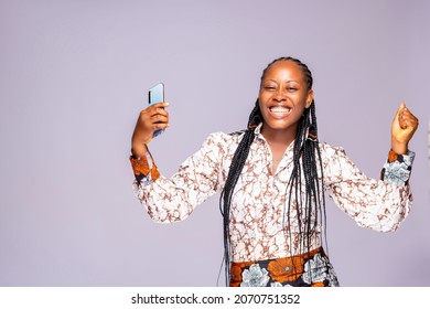 Image of joyful african businesswoman holding cellphone celebrating after winning lottery ticket online isolated over white studio background