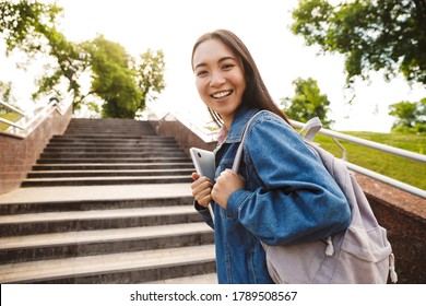 Image Of Joyful Asian Student Woman Holding Laptop And Smiling While Going Up Stairs In Park