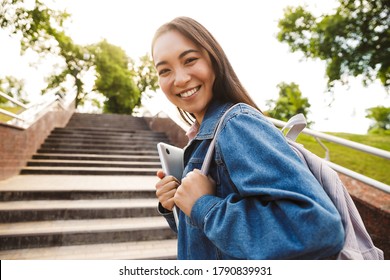 Image Of Joyful Asian Student Woman Holding Laptop And Smiling While Going Up Stairs In Park