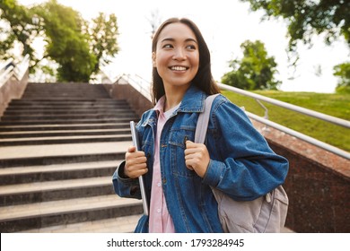 Image Of Joyful Asian Student Woman Holding Laptop And Smiling While Going Up Stairs In Park