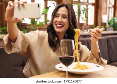 Image of joyful brunette adult woman taking selfie photo on cellphone while having lunch in cafe indoors - Powered by Shutterstock