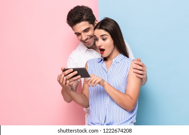 Image of joyful couple 20s smiling and looking at mobile phone isolated over colorful background