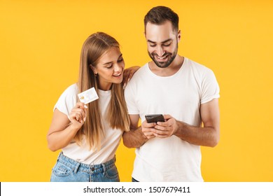 Image of joyful couple man and woman smiling while holding smartphone and credit card isolated over yellow background
