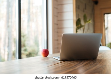 Image of laptop computer on table indoors near apple and window.