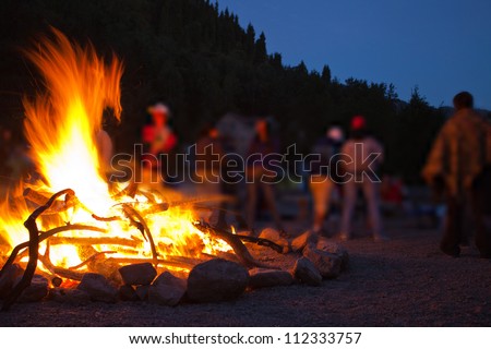 Image of a large campfire, around which people basking in the mountains at night
