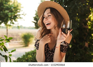 Image of laughing young woman sitting in cafe outdors in park holding glass drinking wine.