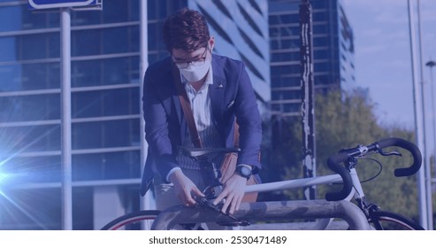 Image of light spots over asian man with face mask locking bicycle. national bike to work day and celebration during covid 19 pandemic concept digitally generated image. - Powered by Shutterstock