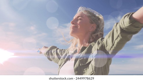 Image of light spots over caucasian woman with arms outstretched. never give up day and celebration concept digitally generated image.