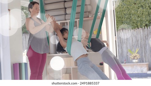 Image of light spots over two diverse teenage girls doing aerial yoga and relaxing at home. Friendship, youth, free time, wellbeing, fun and healthy lifestyle, digitally generated image. - Powered by Shutterstock