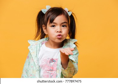 Image Of Little Girl Child Standing Isolated Over Yellow Background. Looking Camera Blowing Kisses.