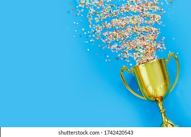 Image Of Little Gold Cup , Concept For Winning Or Success. Golden Trophy Cup And Streamers On Blue Background, Top View With Space For Text