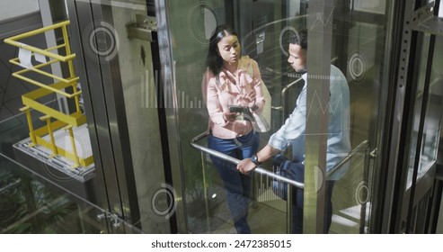 Image of loading circle, diverse coworkers discussing reports on digital tablet in elevator. Graphs, digital composite, business, progress, planning, teamwork and technology concept. - Powered by Shutterstock