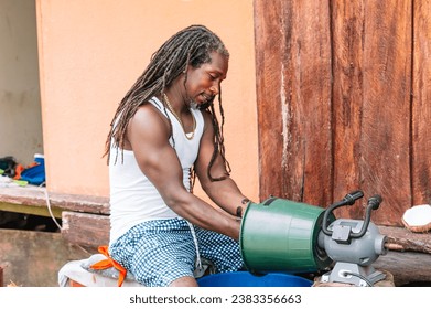 Image of long-haired African-American man with long braids working in his enterprise shredding coconut with a homemade machine. - Powered by Shutterstock