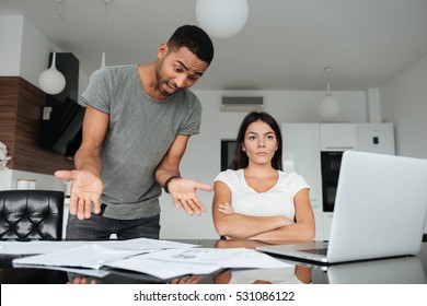 Image of loving couple discussing about domestic bills at home. Woman seriously look aside. Man screaming to woman while holding documents.