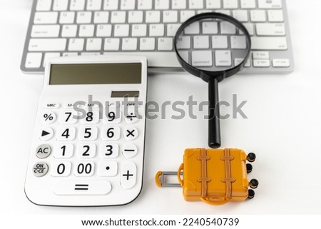 An image of making a reservation for a trip on a computer. A keyboard, a carrying case and a magnifying glass.