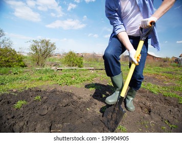 Image of male farmer in rubber boots didgging in the garden